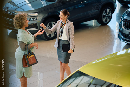 Happy saleswoman giving car key to her female customer in showroom.