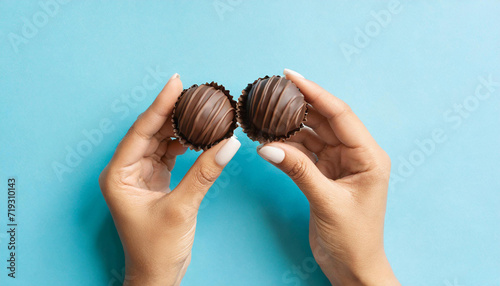Young adult woman hand fingers holding fresh and old spoiled dark chocolate candies on light blue table background. Pastel color. Compare two pralines. Point of view shot. Top down view