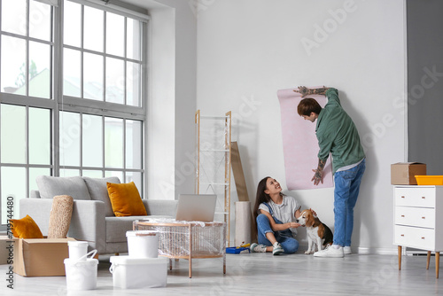 Young couple with Beagle dog wallpapering during repair in their new house
