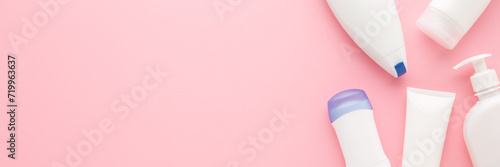 Different white plastic cosmetic bottles on light pink table background. Pastel color. Care about clean and soft body skin. Beauty product. Closeup. Wide banner. Empty place for text. Top down view.
