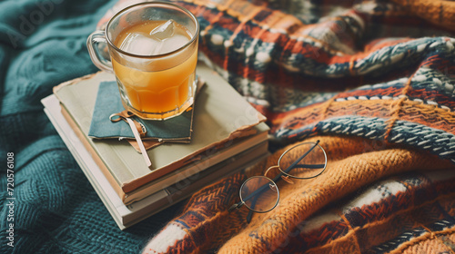 A flat lay of summer reading essentials including a stack of books reading glasses a bookmark and a cup of iced tea on a cozy blanket.
