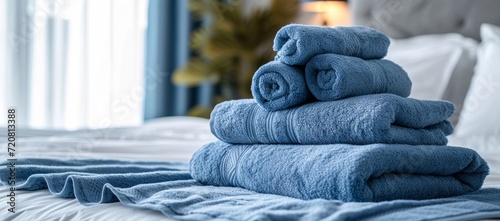 A cozy indoor bed adorned with a stack of soft blue linens, including towels, cloths, and blankets, invites relaxation and comfort