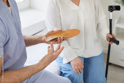 Male doctor podiatrist gives comfortable orthotic insoles for orthopedic shoes to an overweight woman patient with crutches who has had a leg and foot injury. Crop shot