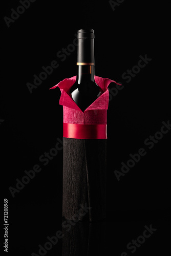 Bottle of red wine wrapped in crepe paper on a black background.