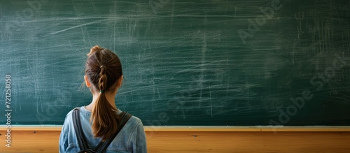 Teacher erases blackboard in vacant classroom, rear view.