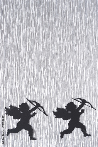 two black paper cupid silhouettes on silver crepe paper with crinkled texture