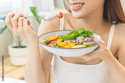 Diet concept, happy asian young woman hand use a fork to prick tomato, fresh vegetable or green salad, eat nutrition food on table at home, low fat to good body. Girl getting weight loss for healthy.