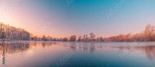 Calm lake water reflections forest trees panoramic sunrise sky. Beautiful silence morning dawn in early spring late winter. Soft bright pink purple colored sky panorama. Beautiful nature landscape