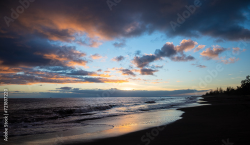 A sunset on Waimea Beach on Kauai reflects warmth onto gentle waves and a glow on the dark sand.