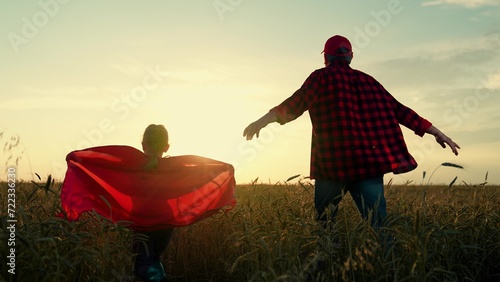 Dad of daughter plays superheroes in wheat field. Dad child run around in red raincoats, playing outdoors. Family carnival in field, Halloween. Dad, girl dreams of becoming superhero, fly in red cape