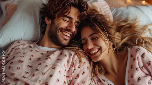 A happy couple in matching pajamas laughs while lying in bed