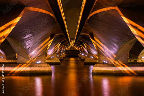Golden symmetrical lights under a modern concrete bridge over a river