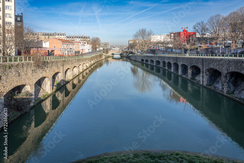 Paris, France - 01 27 2024: Lock n°1 Canal St Denis. Reflections on the Saint-Denis Canal, a train on a bridge from Flanders Bridge Lock reflecting.