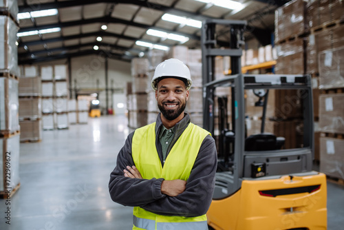 Portrait of warehouse worker standing by forklift. Warehouse worker preparing products for shipmennt, delivery, checking stock in warehouse. Banner with copy space.