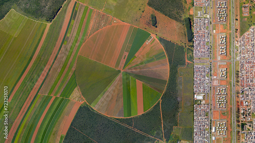 Food safety and population, circular fields and city border, looking down aerial view from above, bird’s eye view center pivot irrigation system and city side by side, Brazilya, Goias, Brazil