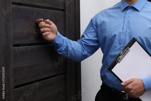 Collection agent with clipboard knocking on wooden door, closeup