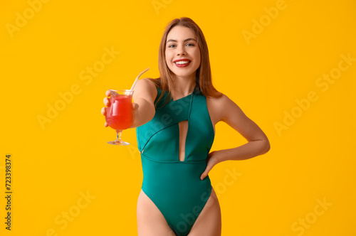 Beautiful young woman in tank swimsuit and with cocktail on yellow background