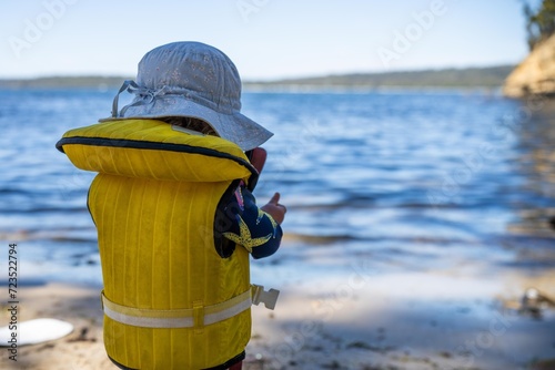 toddler wearing a lifejacket in a kayak on a sandy beach on holiday in summer in australia
