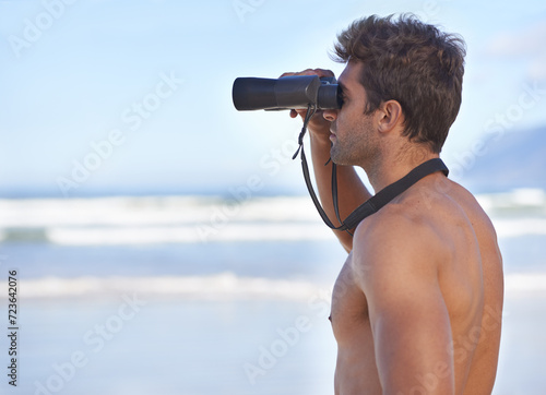 Man, binoculars and lifeguard on beach in search or checking danger for health and safety. Face of male person in fitness for security, bay watch or patrol by the ocean coast or sea in surveillance
