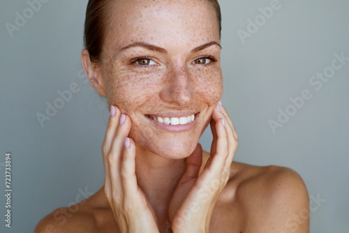 Freckles. Portrait of a young woman is posing with a chin look against grey background. Natural beauty and glowing clean hydrated skin