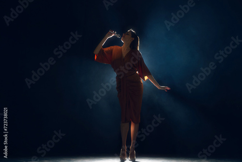Female silhouette, singer under glowing bright spotlights at stage in smoke against black background. Concept of hobby, festival, concert, lifestyle, disco, entertainment. Ad