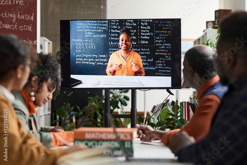 Black woman as professor on computer screen giving online class via remote technology to group of students