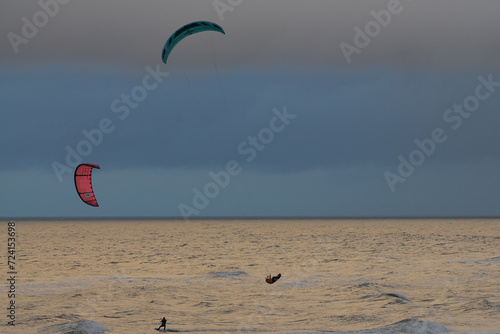 Kitesurfing. Kiteserferzy o zachodzie słońca na tle złocistego morza. Silny wiatr tworzy doskonałe warunki do powietrznych ewolucji. Pastelowe kolory, low key.