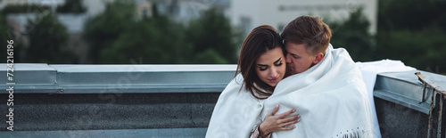 Beautiful young loving couple on a surprise romantic date on a roof top. Picturesque view, skyscrapers on background. Wine, candles, kisses on holiday Saint Valentine's Day celebration outdoors