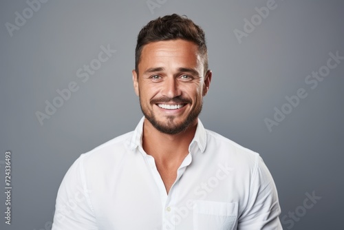 Handsome young man in white shirt smiling and looking at camera while standing against grey background