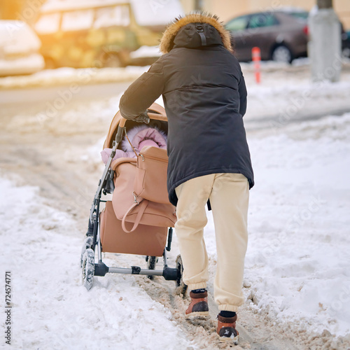 Man pushing baby carriage on snowy road after blizzard. Father walks with baby stroller on snowy sidewalk in winter season. Trendy man push baby stroller wheels get stuck in the snow. Selective focus