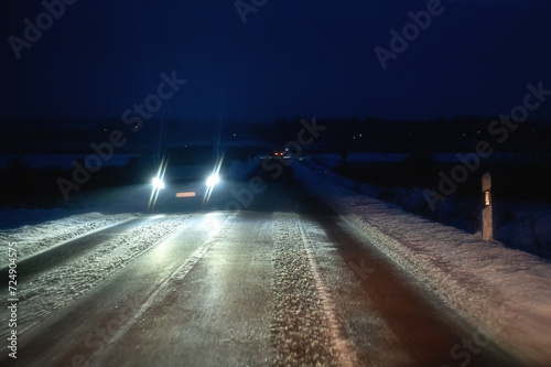 Licht vom Gegenverkehr blendet auf eisiger Fahrbahn im Winter bei Nacht