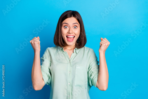 Portrait of overjoyed girl with stylish hairdo wear turquoise blouse clenching fists scream win bet isolated on blue color background