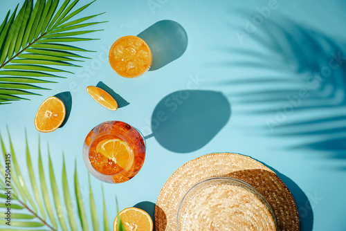 Summer refreshing cocktail aperol spritz with orange and palm leaves on a blue background with shadows, top view