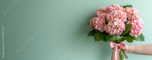 banner,a man's hand holds a large and stylish bouquet of pink hydrangeas with a pink ribbon, on a light green background,on the left there is a place for text,the design concept of festive materials