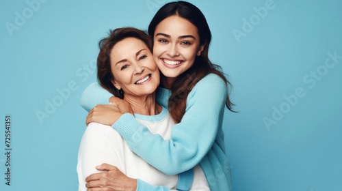 Happy mother and daughter hugging and looking at camera isolated on blue background