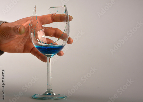 niebieski płyn w peknietym kieliszku do wina, dłoń trzymajaca pęknięty kieliszek, blue liquid in broken wine glass, hand holding broken wine glass,hand with broken wine glass with blue liquid