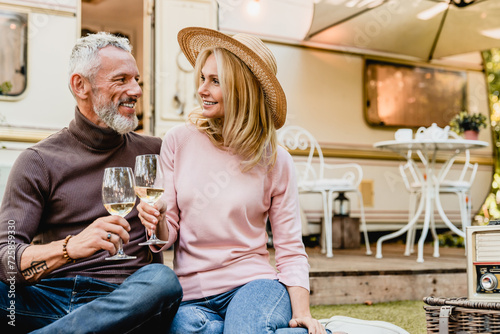 Senior couple on a date during picnic looking at each other with love drinking wine in the porch of their camper van. Spouses celebrating anniversary on a trip holiday by trailer motor home