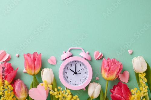 Time to celebrate International Women's Day. Top view photo of alarm clock, hearts, tulips, mimosa on turquoise background with space for festive text