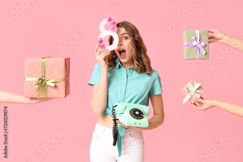 Young woman with retro telephone, figure 8 made of paper and hands holding gift boxes on pink background. International Women's Day