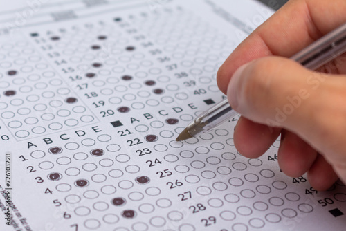 Hand filling out an exam answer sheet with a pen, concept for public and entrance exams.