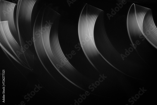 White neon flowing wave of light as trails with smooth stripes on black background, pattern. Abstract background with motion light effect, light painting in disco style.