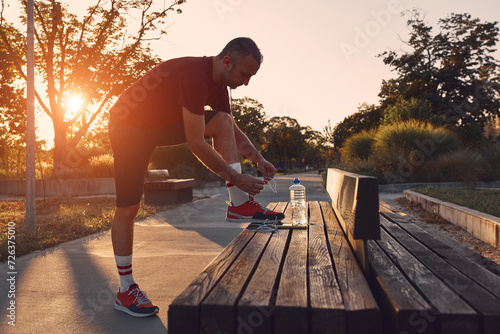 Sporty man tying laces on jogging sneakers in a park.