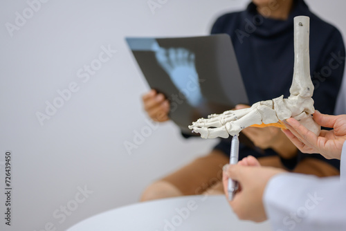 An orthopedic doctor points to a model of ankle and foot bones explaining to a patient a foot bone problem. Health care and spine concept