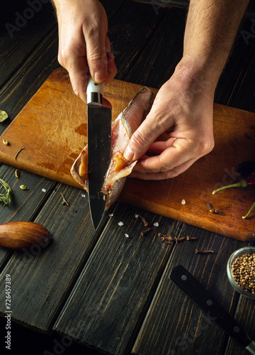 The chef cuts fresh Merluccius fish with a knife on a wooden cutting board. Home-cooked national fish dish according to a unique recipe