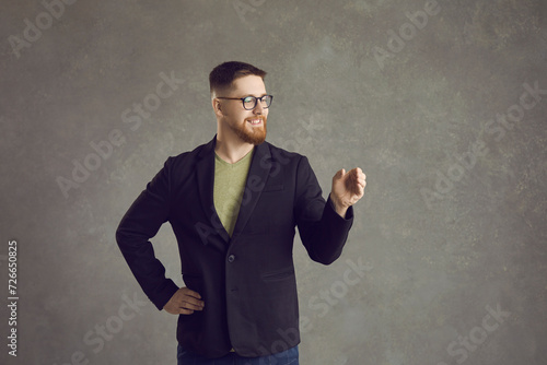 Young person demonstrating stuff. Happy man showing invisible object. Positive hipster guy in suit and glasses holding something like cup or beverage bottle. Concept of people advertising new product