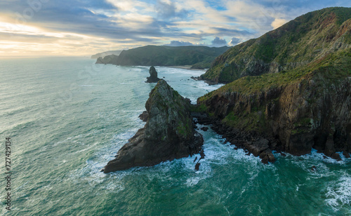 Aerial: Rocky coastline and ocean surf in the waitakere ranges at sunset. Whites Beach, Piha, Auckland, New Zealand.