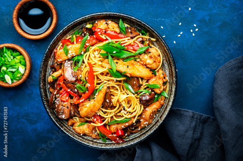 Hot stir fry egg noodles with turkey, paprika, mushrooms, chives and sesame seeds with ginger, garlic and soy sauce. Asian cuisine dish. Blue table background, top view