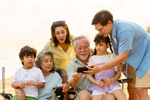 Group of Multi-Generation Asian family enjoy and fun outdoor lifestyle travel ocean together on summer holiday vacation. Happy family using mobile phone taking selfie together on the beach at sunset.