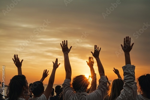 group of people with their hands up looking at the sunset