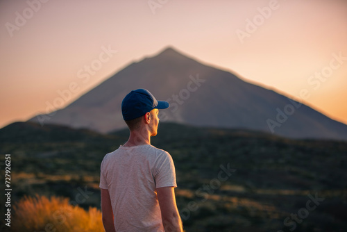 Rear view man looking at landscape with Teide volcano at sunset. Tourist during hike on Canary island of Tenerife..